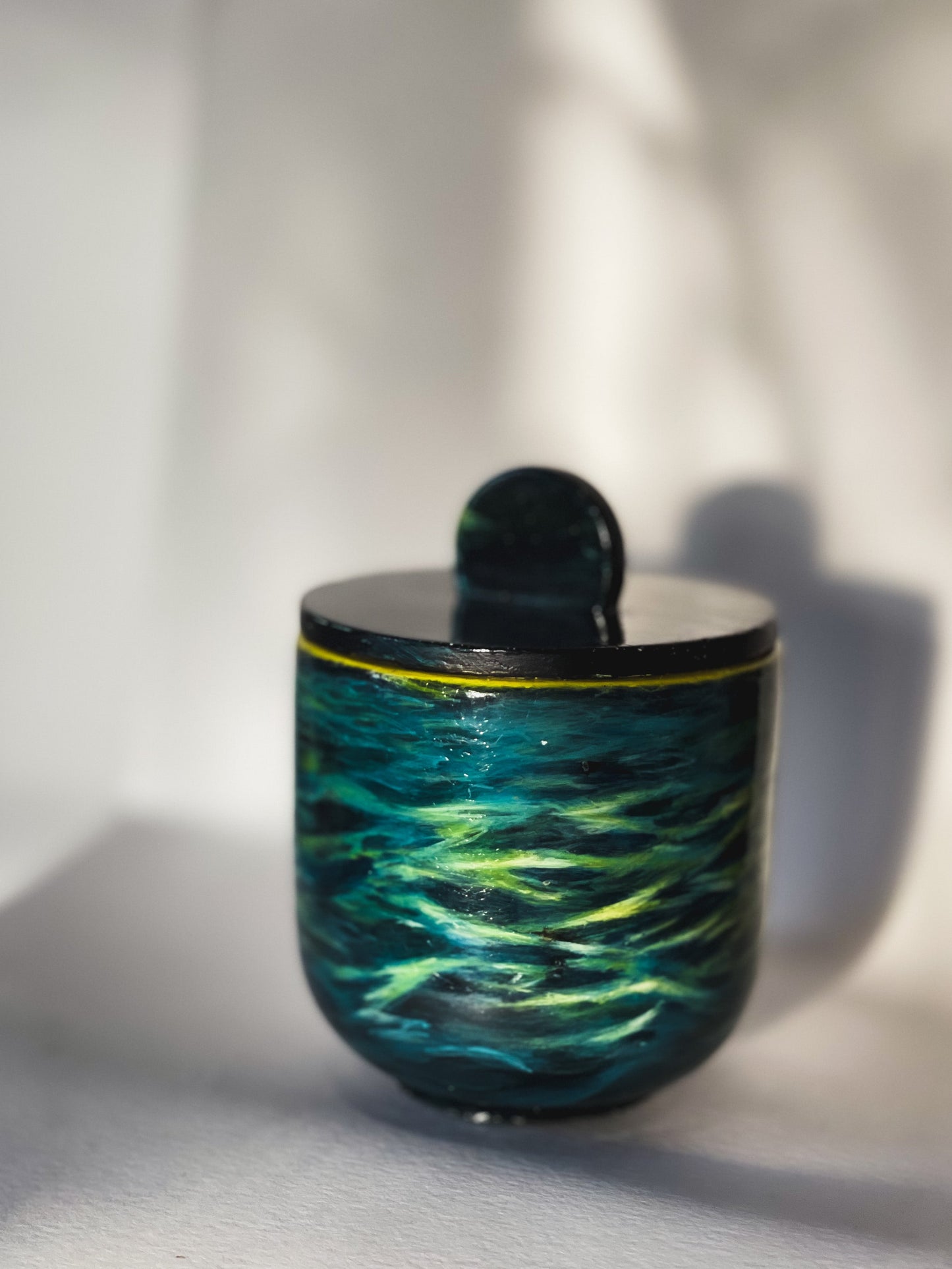 Hand painted concrete jar with a blue / green seascape painted on.background